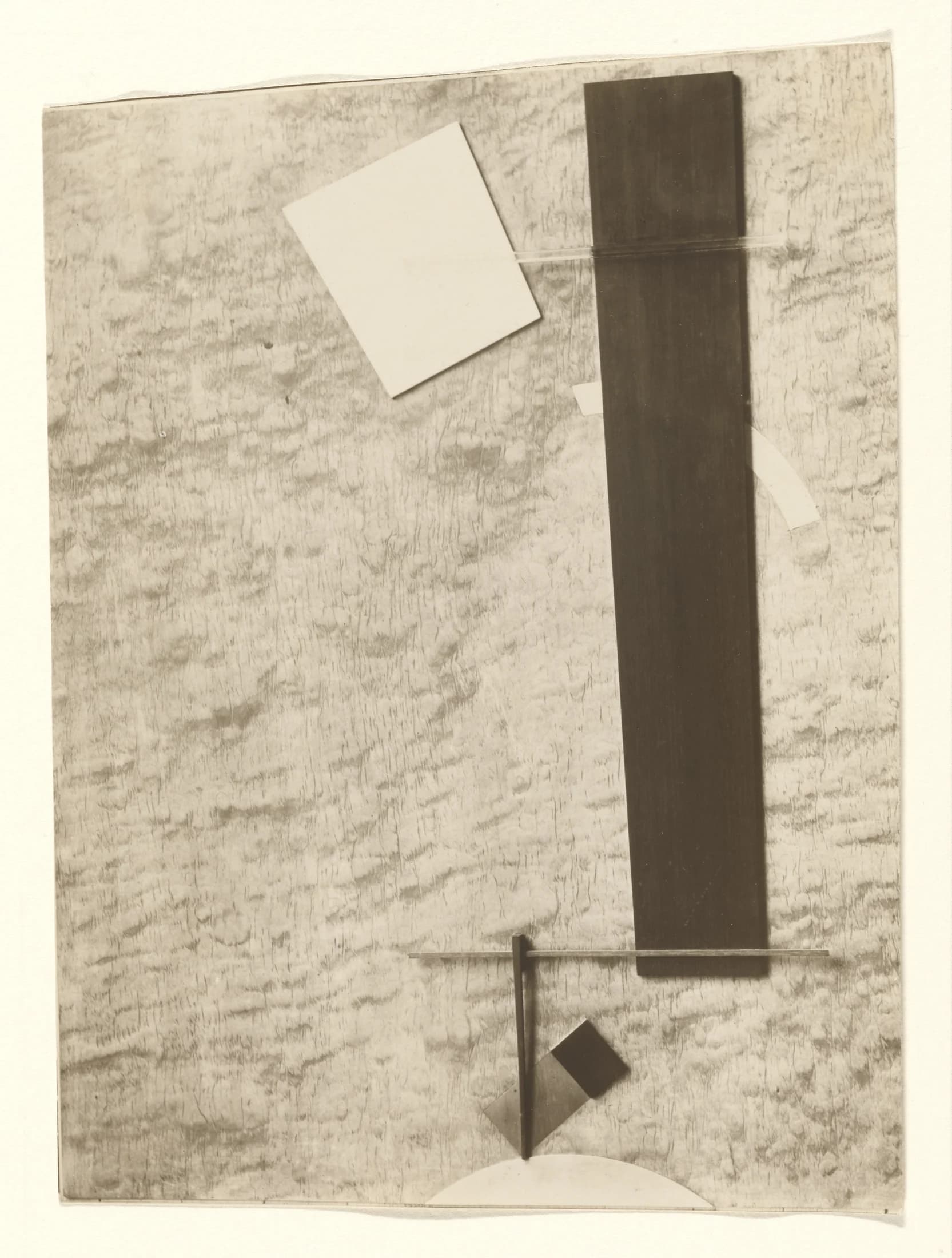 El Lissitzky, Proun No. 83, 1924, gelatin silver print: a photograph of a Proun construction — a tall dark bar, a tilted pale square and a few thin rods and wedges arranged against a mottled ground.