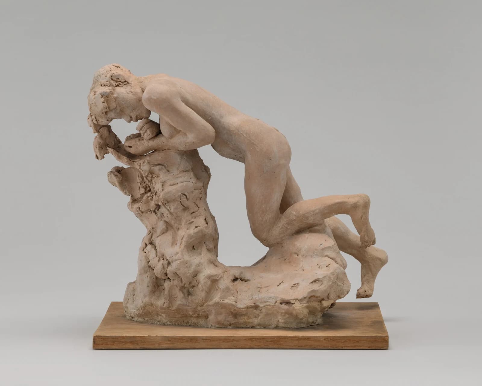 Auguste Rodin, Eve Eating the Apple, c. 1885, terracotta: a figure group on a wooden base photographed against a plain grey ground, a nude figure crouching forward over a roughly modelled rock with its head lowered to its raised hands.